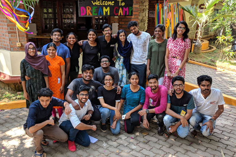 Group picture of happy volunteers in front of Babu terrace inside campus where some are standing and some are sitting on knees